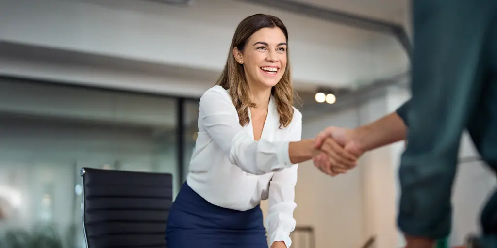 Geschäftsfrau lächelt und gibt einem Kunden im Büro die Hand.