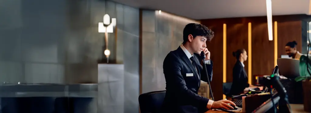 Hotelrezeptionist am Telefon, modernes Interieur, konzentrierte Arbeitsatmosphäre.