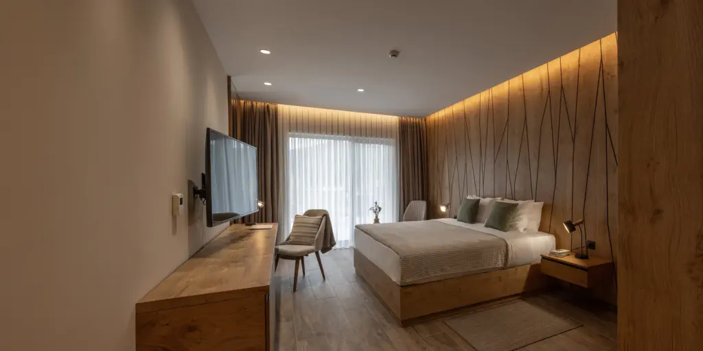 Modernes Hotelzimmer mit Holzverkleidung, großem Bett, Wand-TV und stilvoller Beleuchtung. Elegantes Design und Komfort.