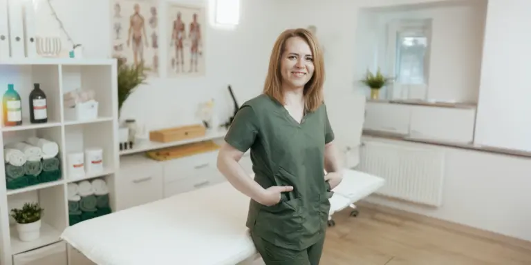 Frau in grüner Kleidung in moderner Praxis mit Regalen und Poster im Hintergrund.